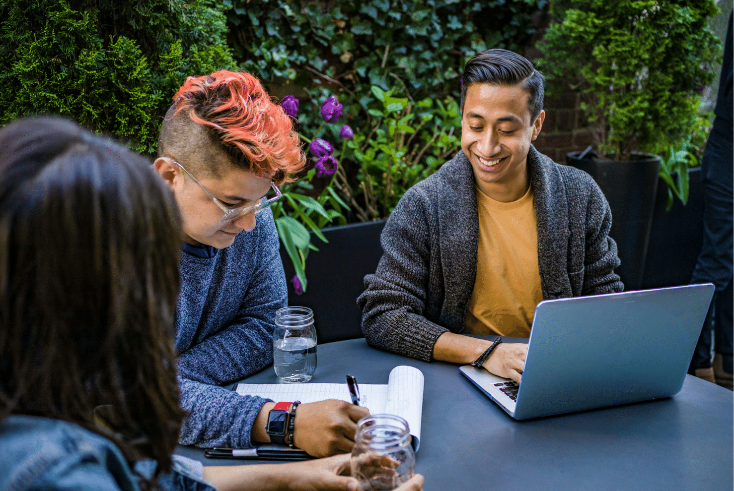 A man on a laptop smiling with two other people next to him working.