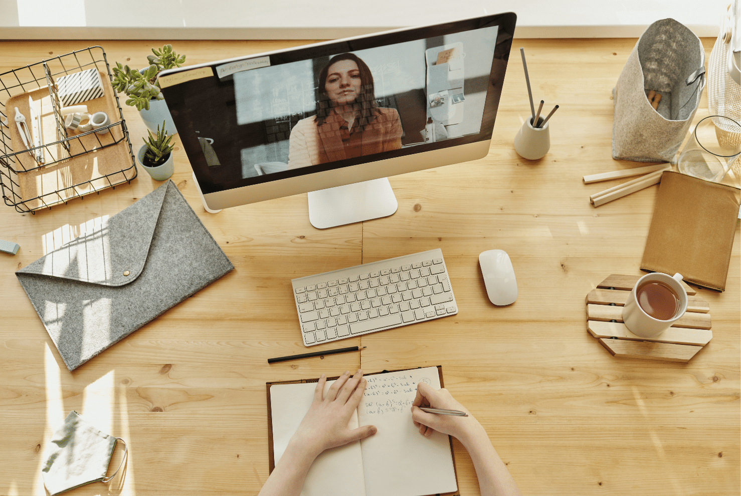 A person out-of-frame video chats with a woman while writing in a notebook.