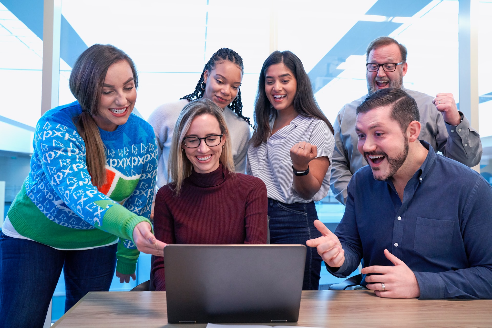 Six smiling adults looking at a laptop while some fist pump and point towards the screen.