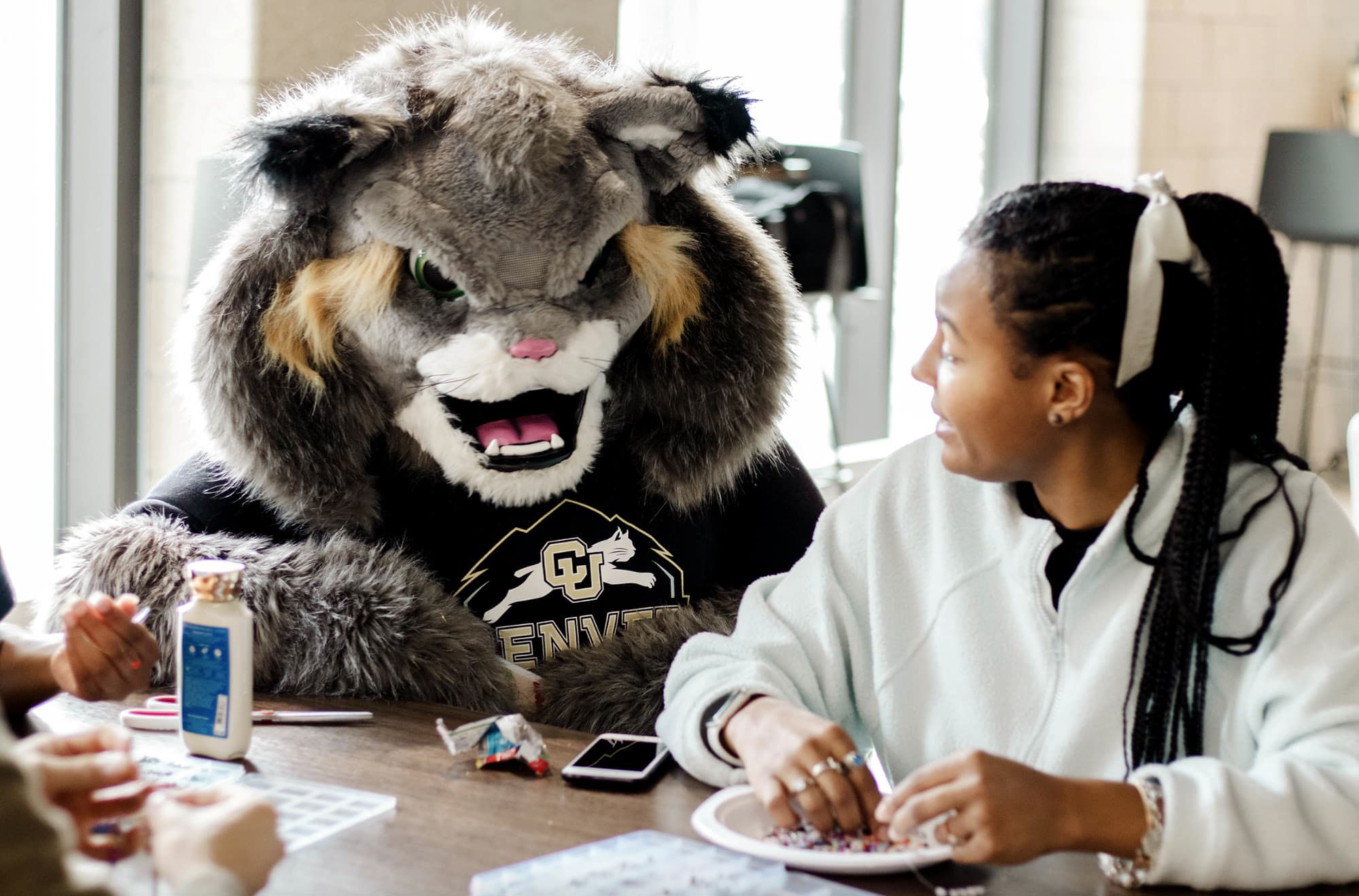 Milo the Lynx and a student make friendship bracelets in the Posner Family Kitchen.