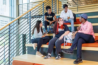 Five students seated on stairs engaging with one another.