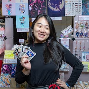 Woman with long black hair smiles while holding up four cards in her hand fanned out.