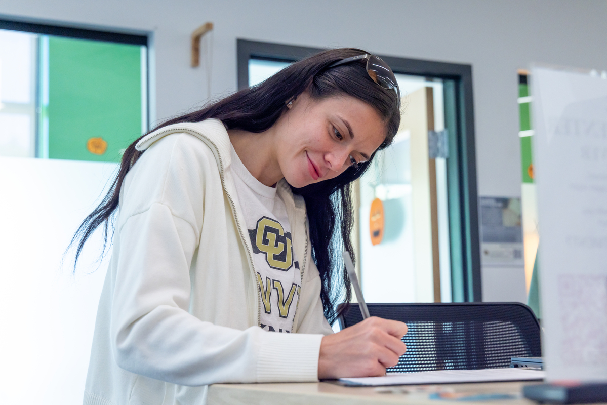 Woman in a CU Denver shirt smiling and writing