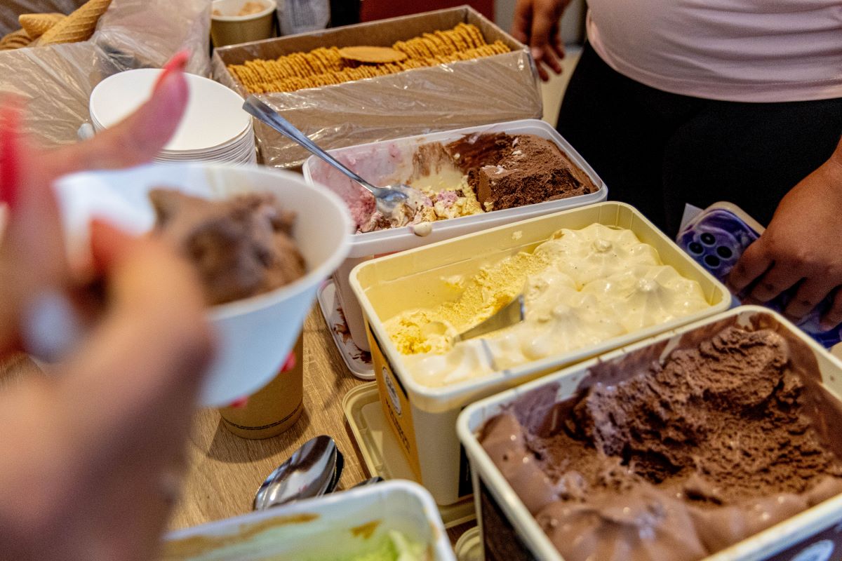 line of ice cream tubs and people holding bowls full of ice cream